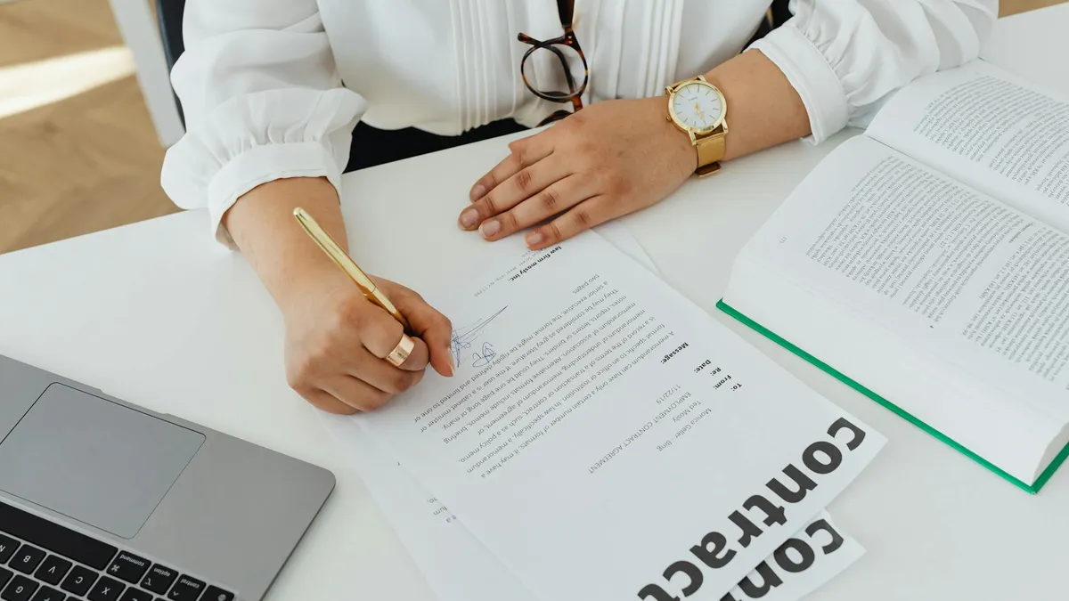 Businesswoman signing a contract at her desk with a laptop