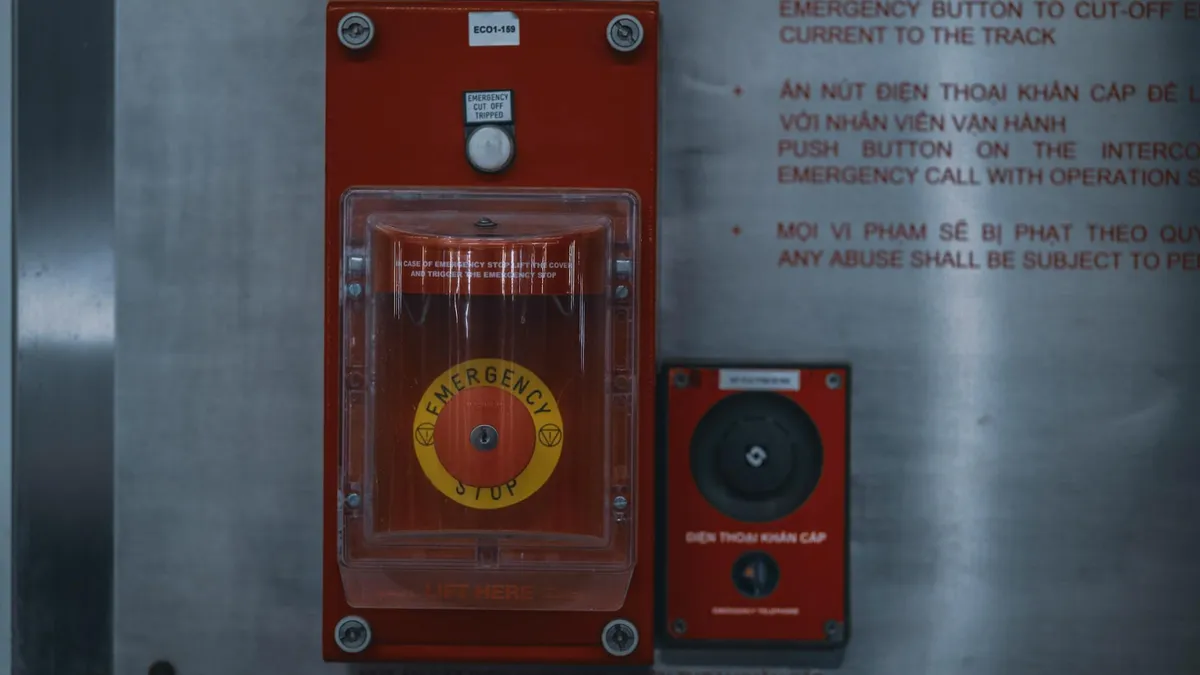 Close-up of a red emergency stop button on an industrial control panel, with warning text partially visible.
