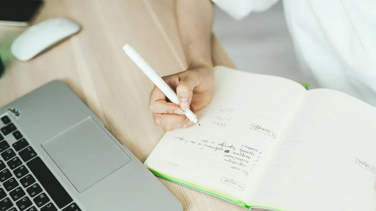 Persona escrivint en un ordinador portàtil amb una llibreta de notes al costat