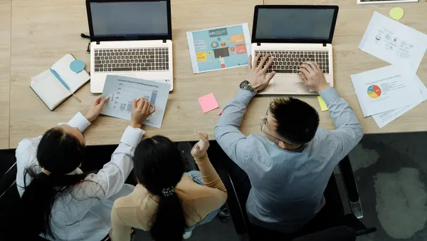 Three colleagues working with laptops and documents at an office table